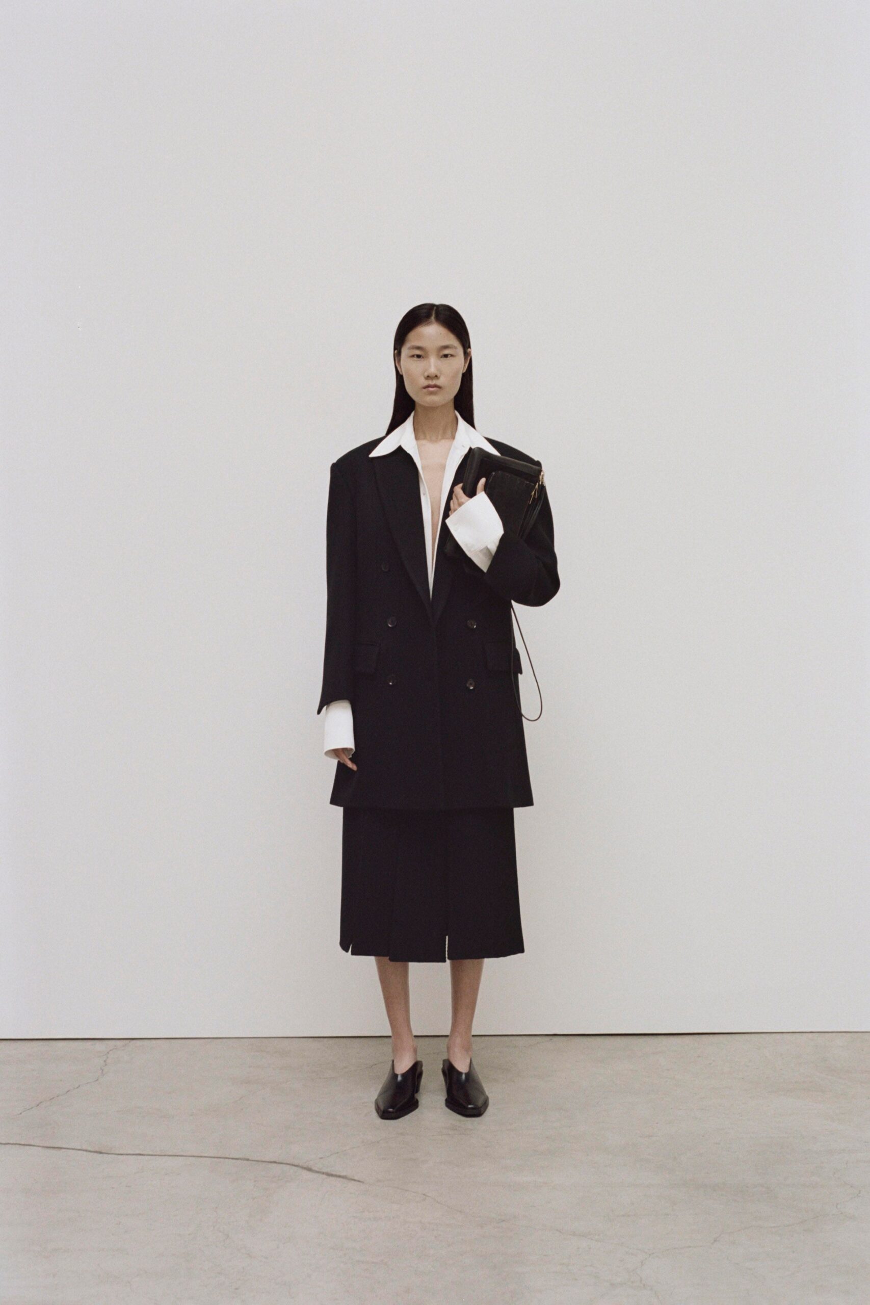 An oversized black blazer with long sleeves and a collared neckline paired with a matching skirt.