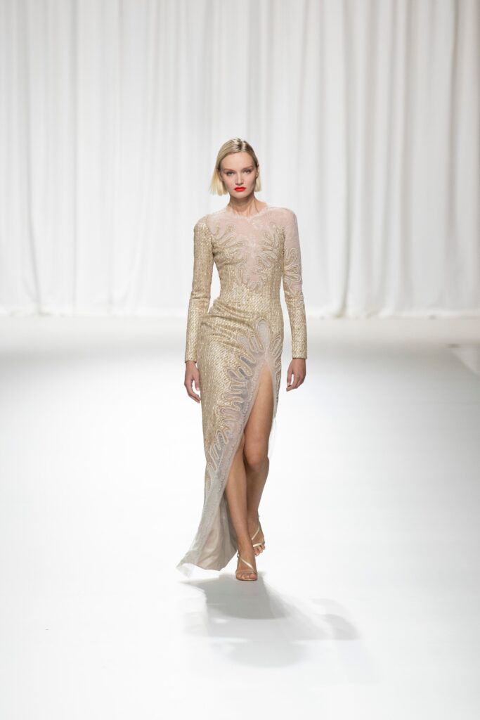 A fitted gold silk gown with long sleeves, a V-neckline, and an embroidered design featuring a slit.
