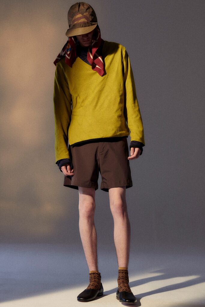 A relaxed yellow long-sleeve top with a V-neck and brown shorts, featuring an asymmetric design.