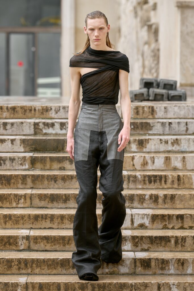 A fitted sleeveless top with an asymmetric design paired with high-waisted black and gray pants.
