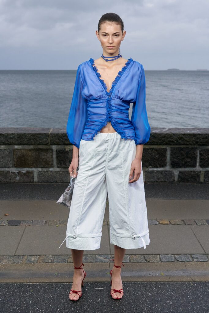 A relaxed blue ruffled blouse paired with white cropped pants, featuring a V-neckline.