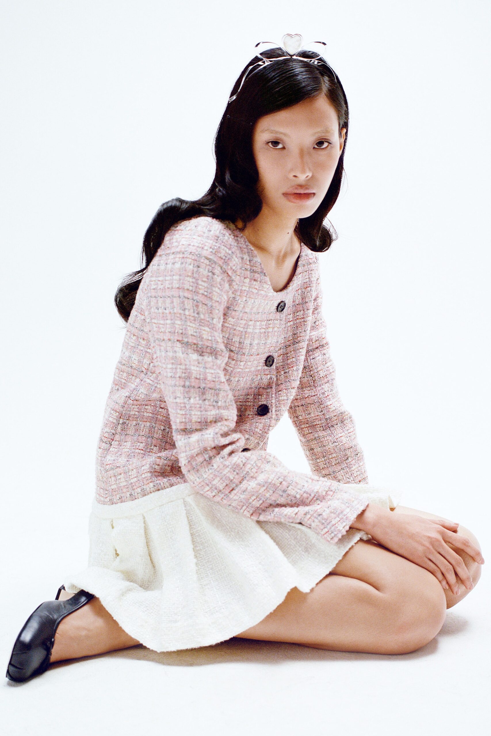 A fitted pink tweed long-sleeve top with a collared design and a pleated white skirt.