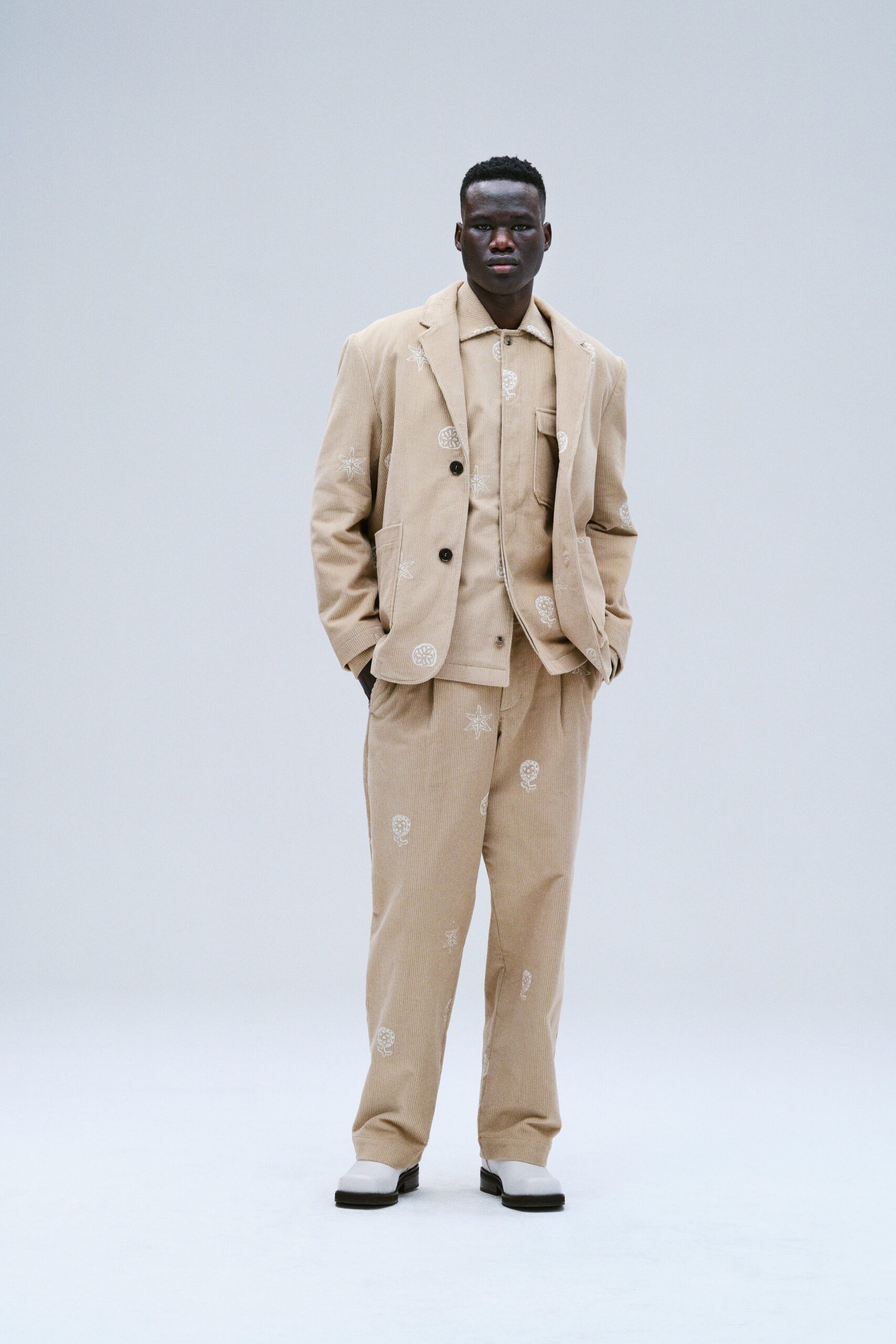 A tailored beige cotton suit with long sleeves and a collared shirt, featuring a printed design.