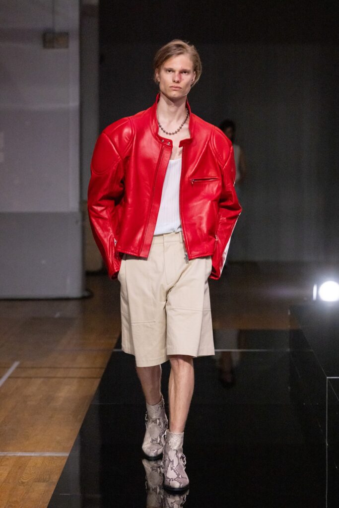 A relaxed fit red leather jacket paired with beige cotton shorts, featuring a collared design and zippered detail.