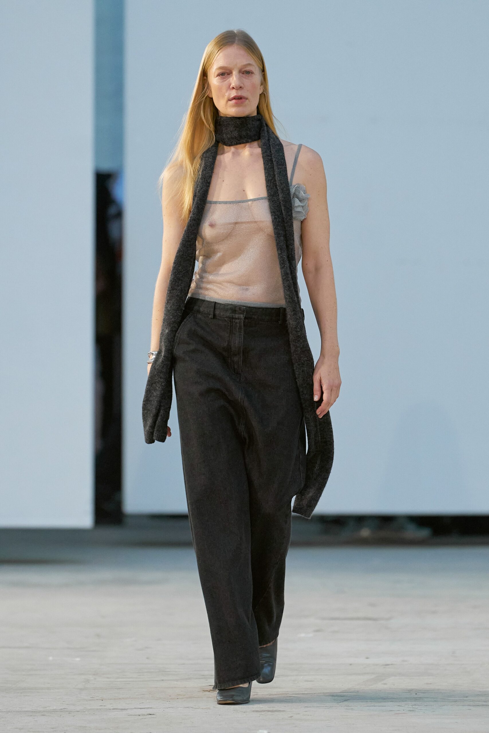 A relaxed beige sheer sleeveless top paired with wide-leg black pants.