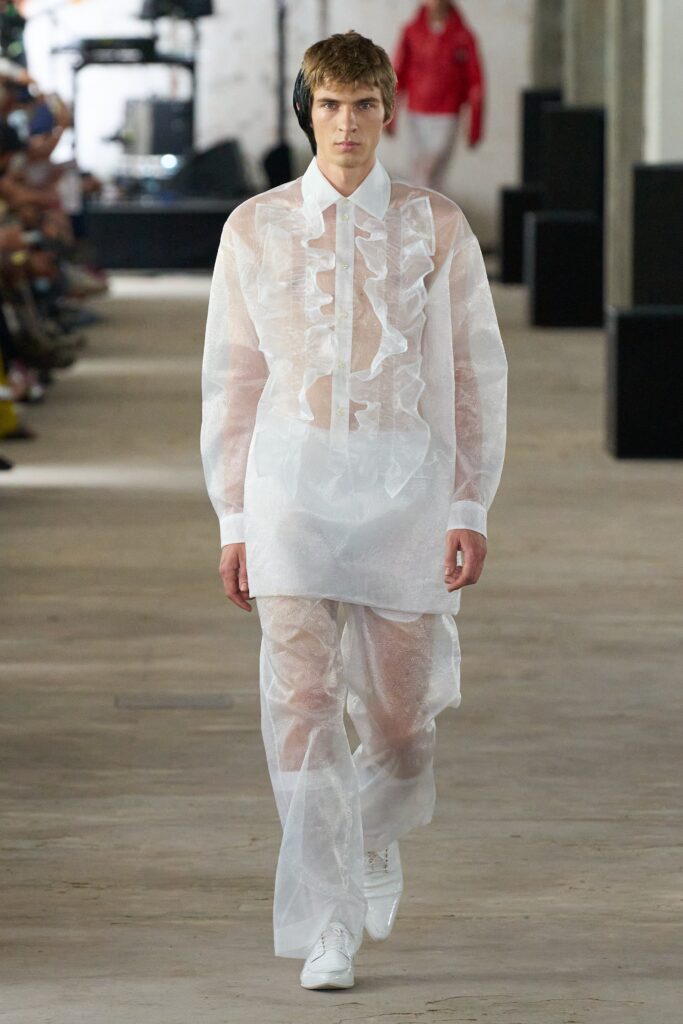 A relaxed white sheer dress with long sleeves, a collared neckline, and ruffled details.