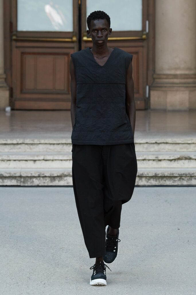 A relaxed black sleeveless top with an asymmetric design paired with loose-fitting black pants.