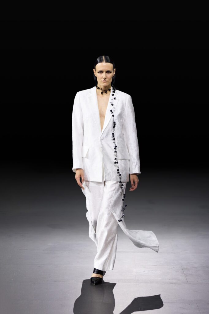 A tailored white silk suit with a longline silhouette and decorative detailing.