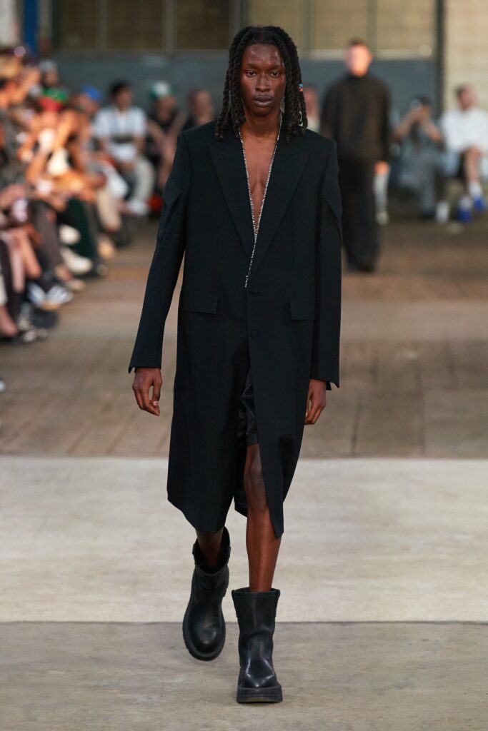 A relaxed black coat paired with shorts, featuring a V-neckline and asymmetric design.