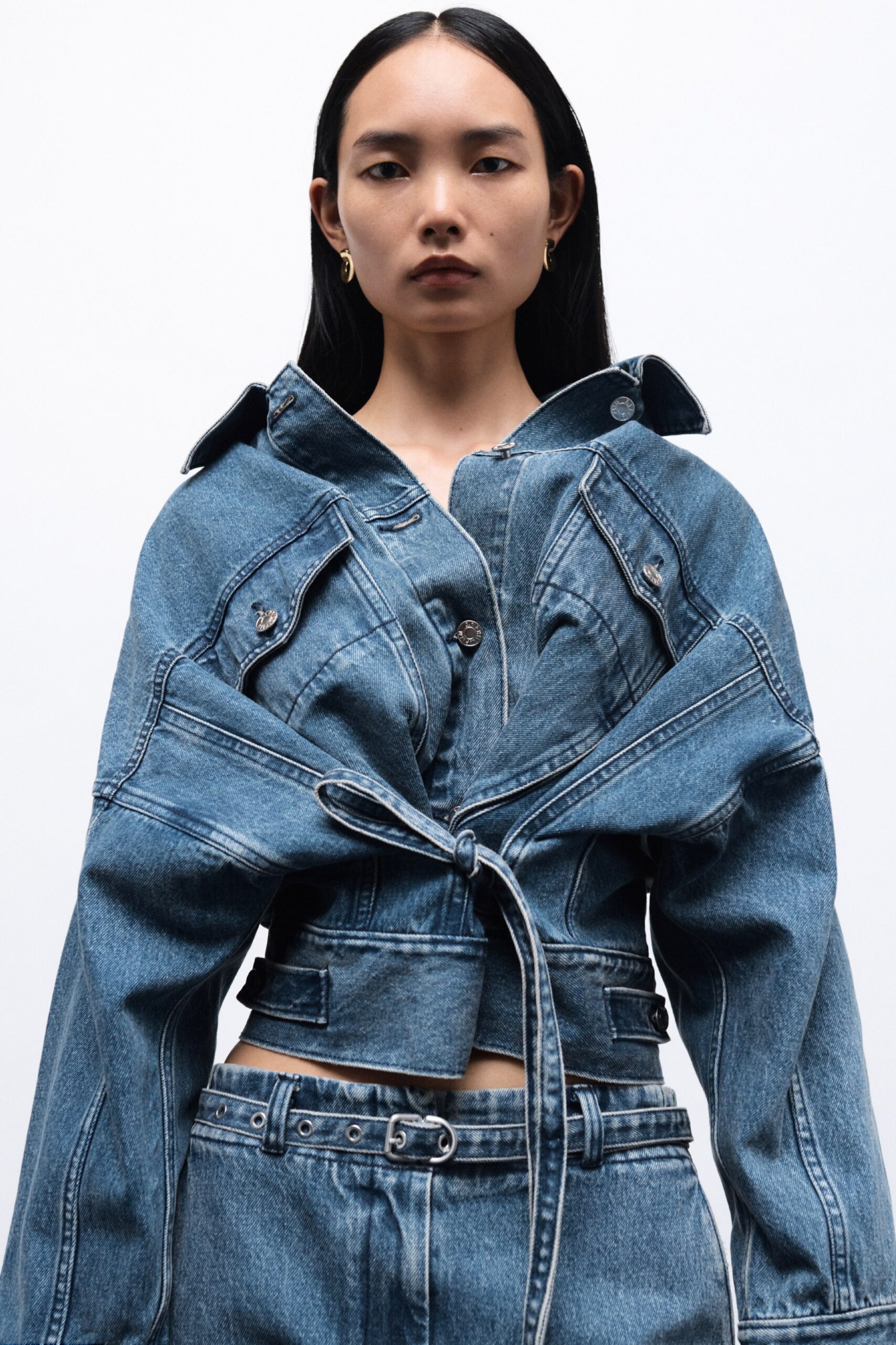A fitted blue denim jacket with long sleeves and an asymmetric design, paired with matching pants.