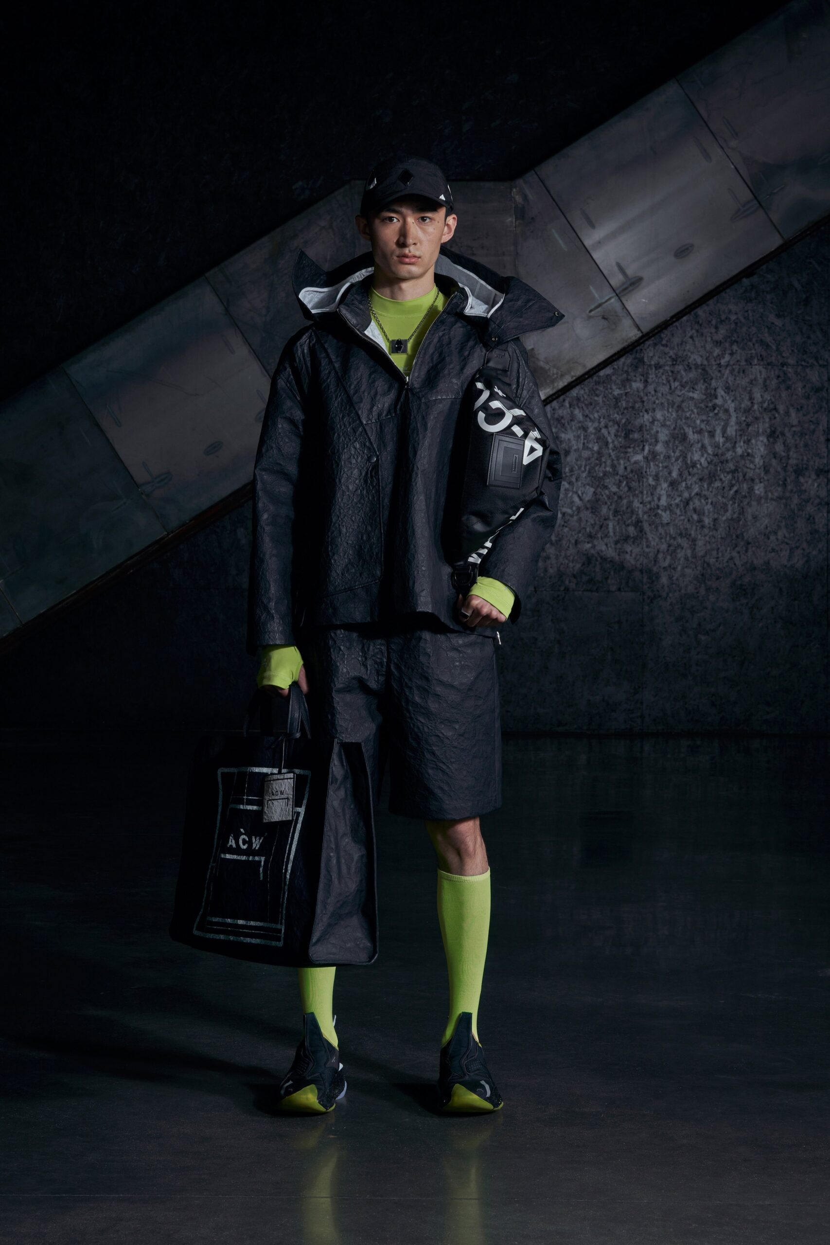 A relaxed black nylon jacket with long sleeves and layered design paired with neon green shorts.