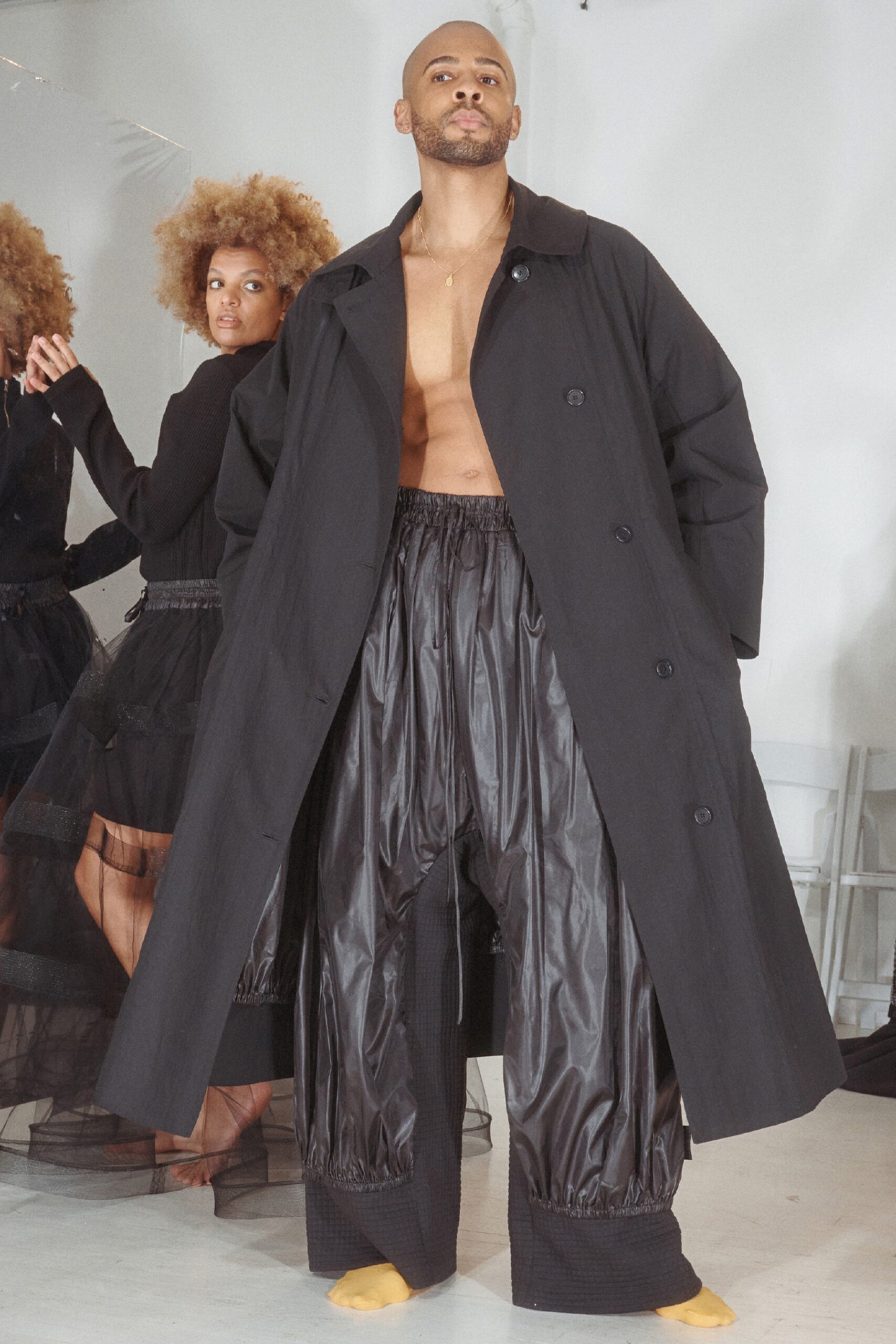 This ensemble features a relaxed black coat with a classic collar, draping effortlessly over wide-leg pants. The pleated design adds a dynamic element, creating movement and depth that enhances the overall silhouette.