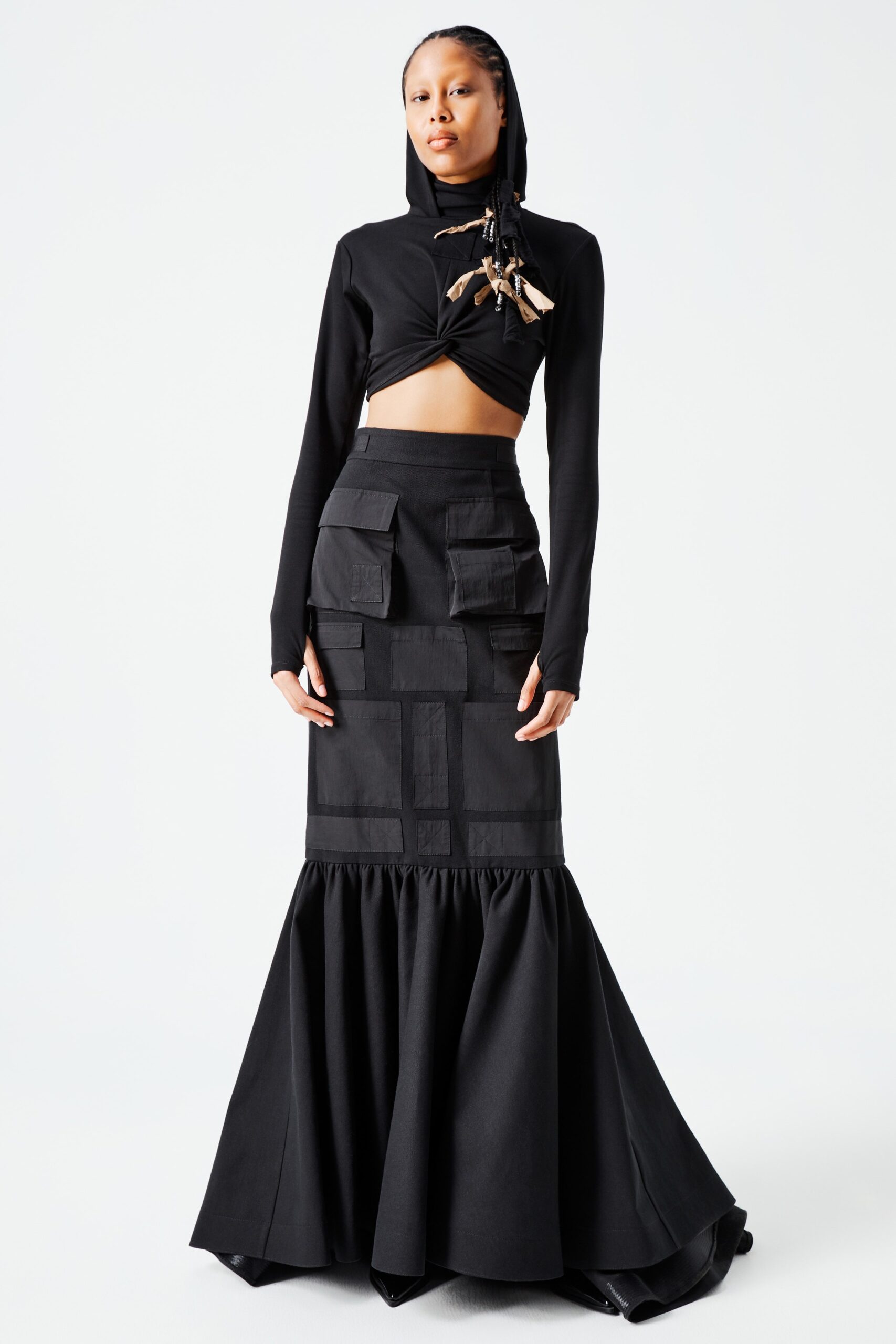 This ensemble features a fitted black top with a high neck and long sleeves, paired with a dramatic flared skirt that adds a sense of movement. The combination of structured elements and flowing silhouette creates a striking contrast, enhancing the overall visual impact.