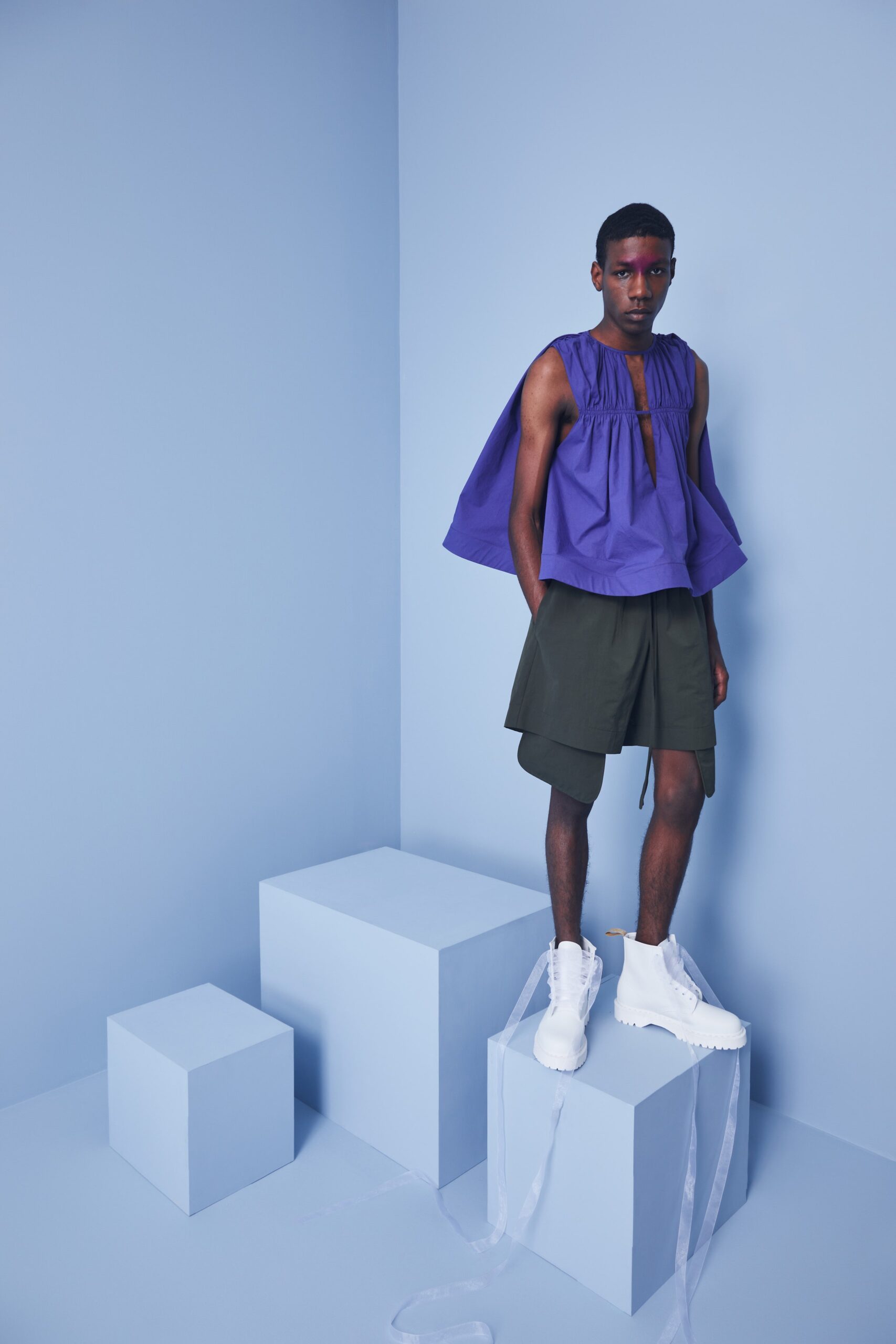 This relaxed sleeveless top features a striking pleated design in a vibrant purple hue, creating a sense of volume and movement. Paired with tailored green shorts, the ensemble balances bold color with contemporary lines, offering a fresh take on casual wear.