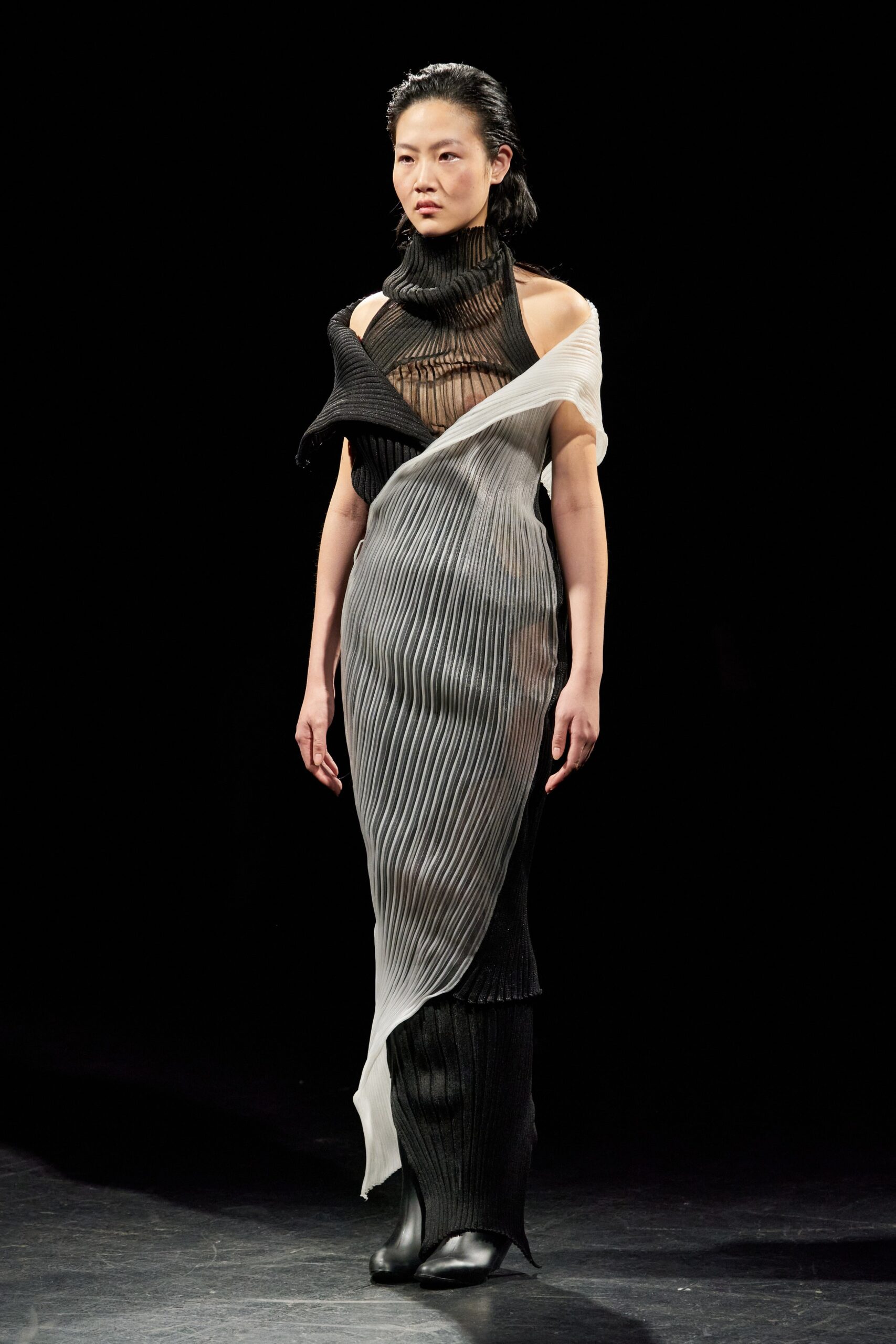 A fitted black and white dress with a high neckline and asymmetric pleated design.