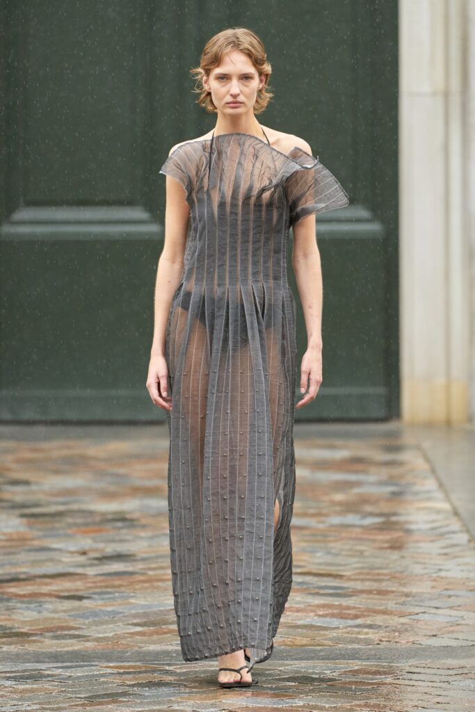 A fitted sheer black dress with a high neckline and pleated, asymmetric design.