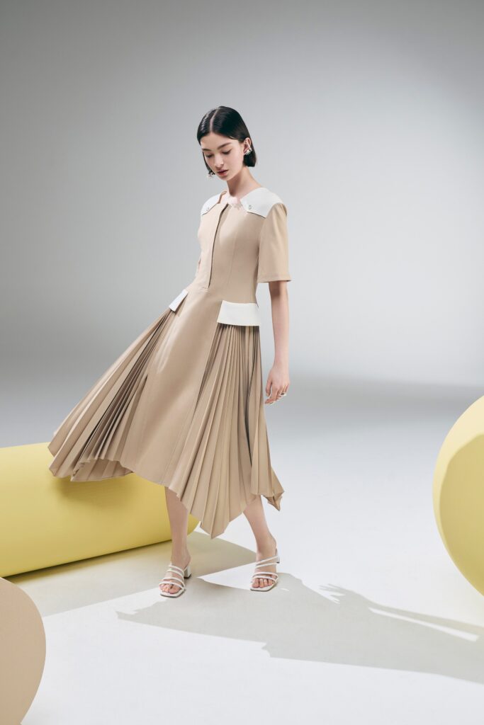 A fitted beige cotton dress with short sleeves, a collared neckline, and pleated A-line design.