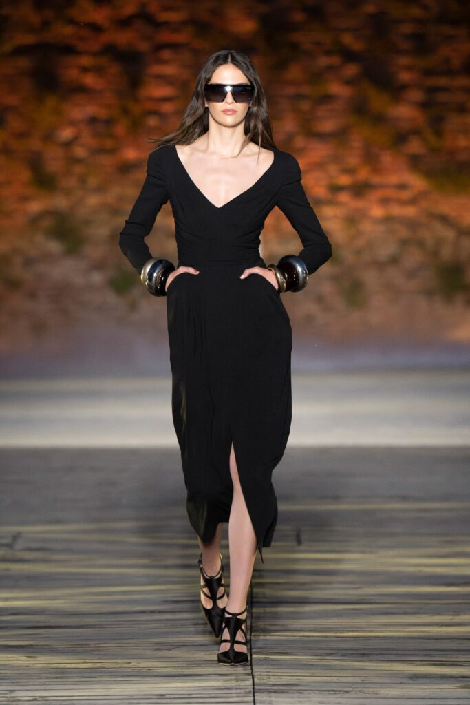A fitted black silk dress with long sleeves, a V-neckline, and a stylish slit detail.