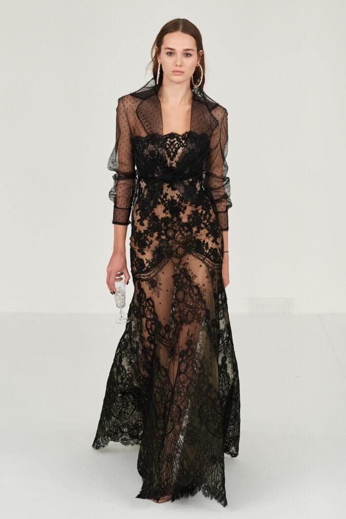 A fitted black lace dress with long sleeves and a V-neckline, featuring sheer and embroidered details.