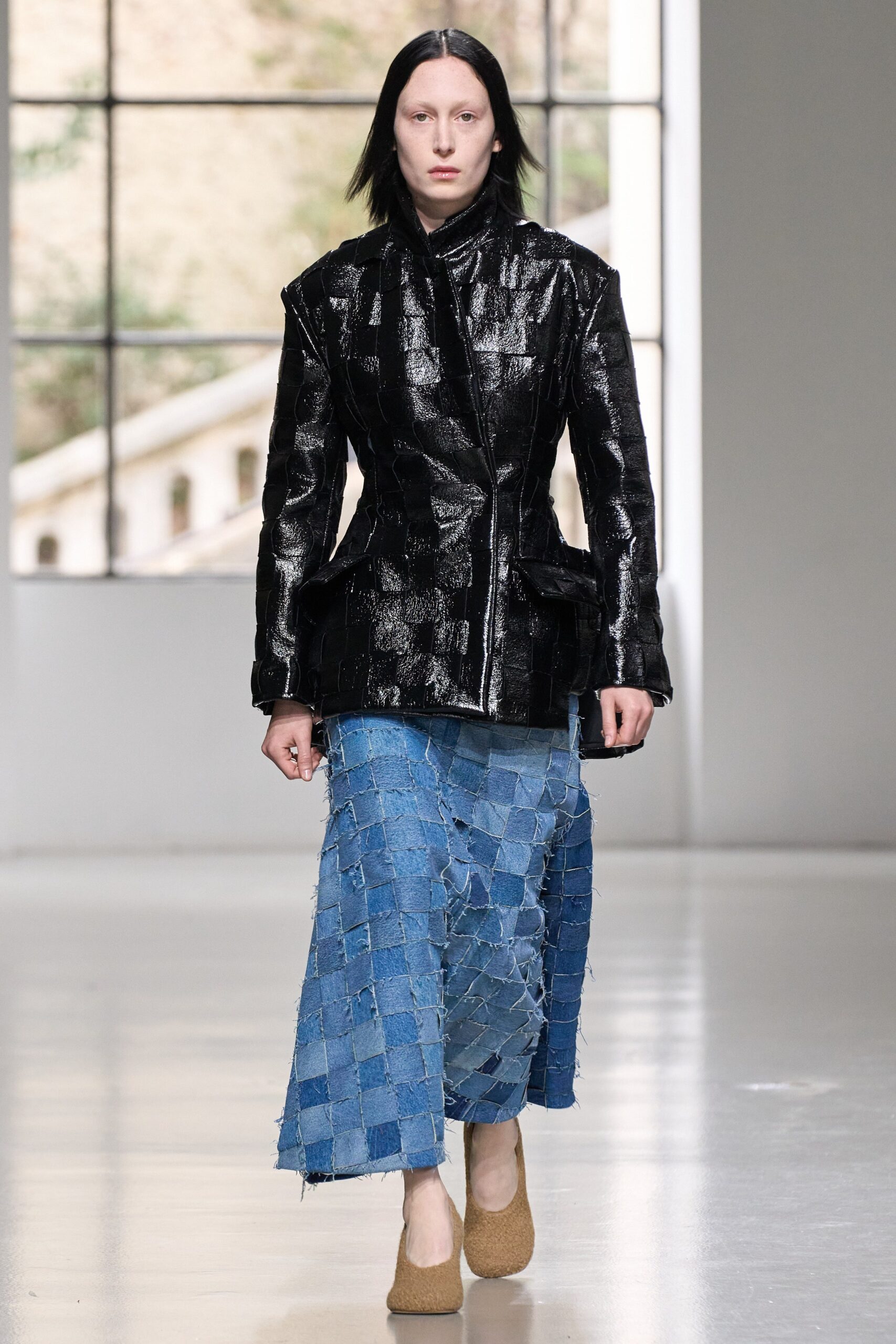A fitted black leather jacket paired with a layered blue denim skirt featuring an asymmetric design.