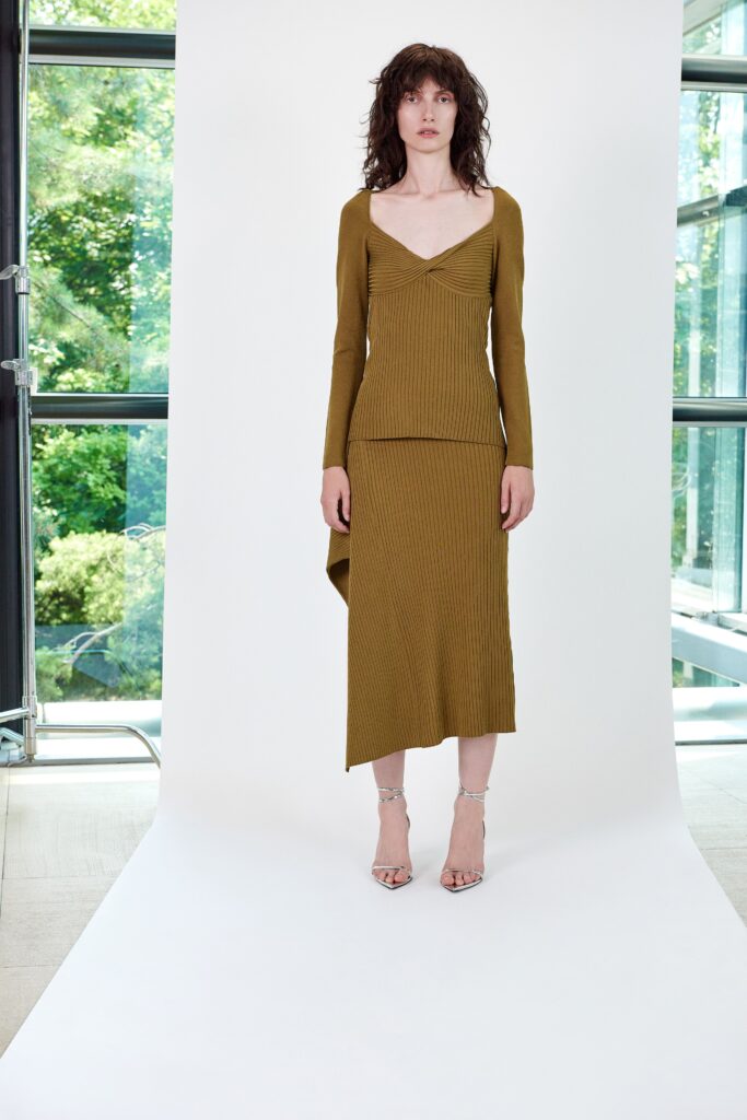 A fitted green long-sleeve dress with a V-neckline and asymmetric hemline.