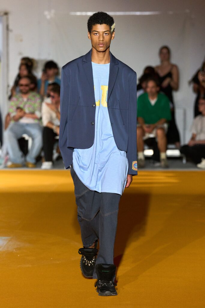 An oversized blue jacket layered over a black t-shirt, creating a relaxed streetwear look.