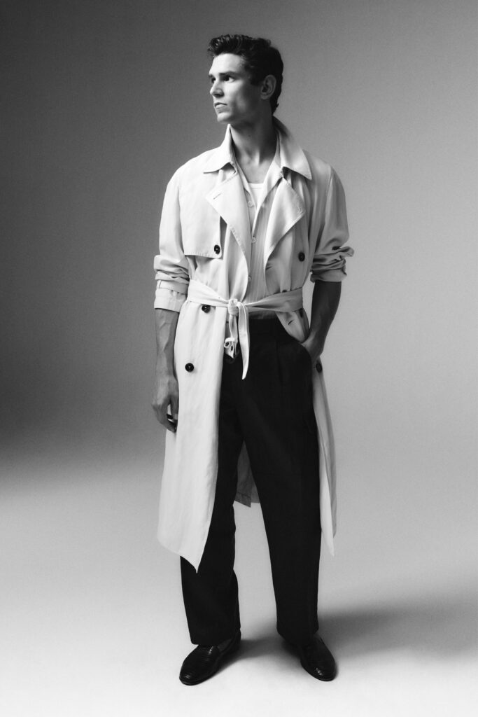 A relaxed-fit beige trench coat paired with black pants, featuring a collared design and buttoned details.