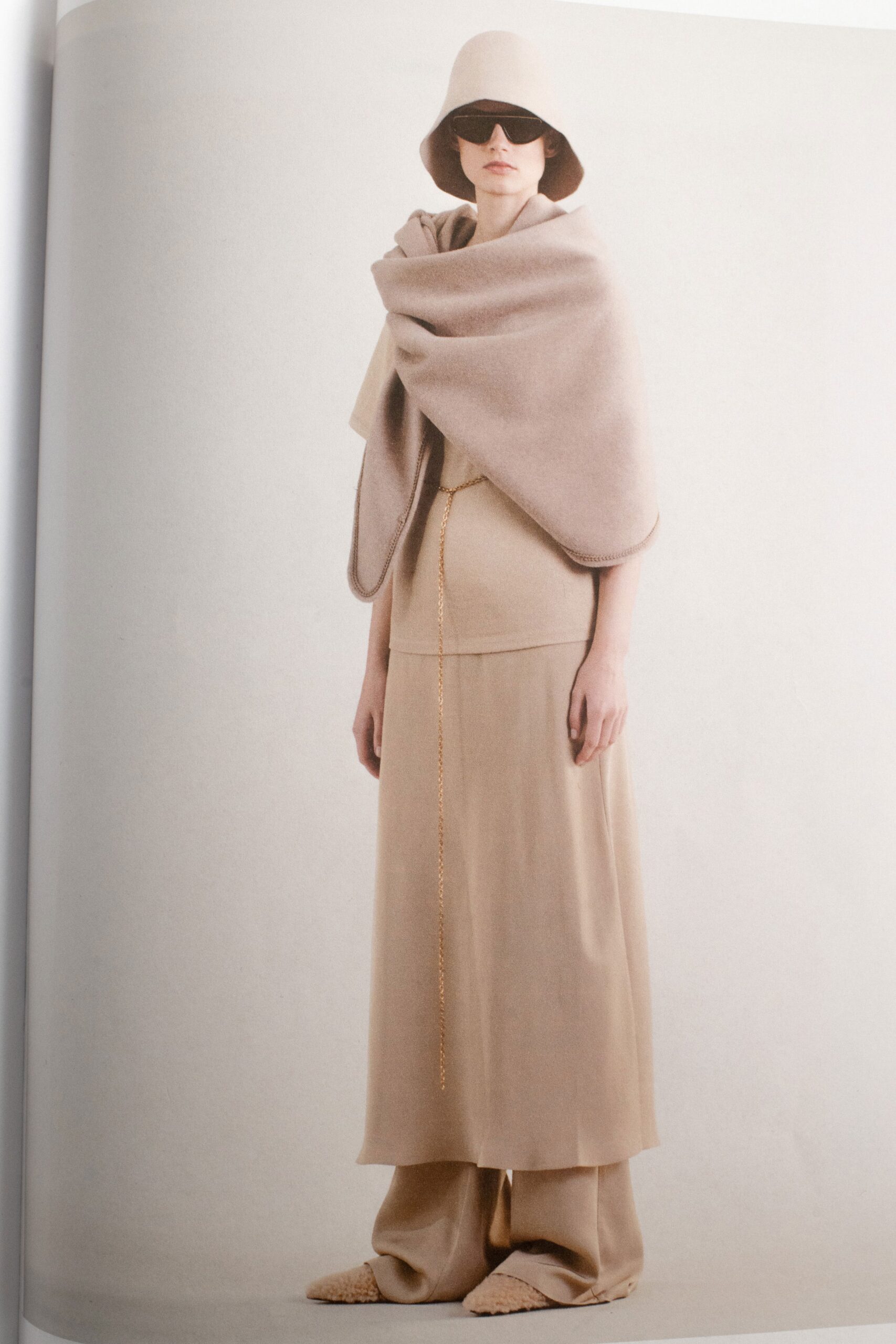 A relaxed beige wool sleeveless dress paired with a matching high-neck cape, featuring a layered design.