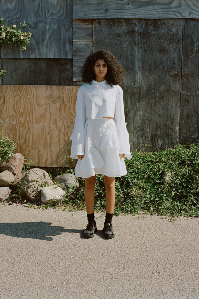 A fitted white long-sleeve top with a collared design paired with an asymmetric layered skirt.