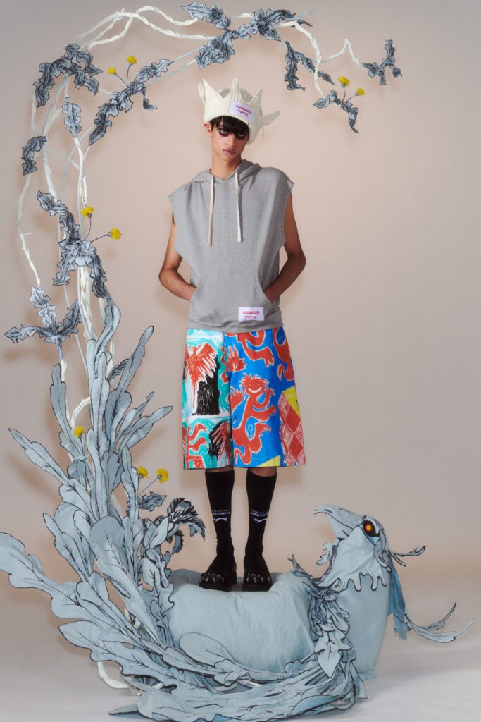 A relaxed gray sleeveless hoodie with printed multicolor shorts.