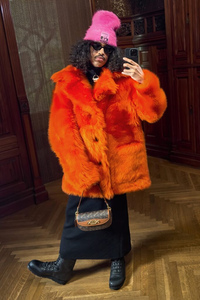 An oversized orange fur coat layered over a black dress, featuring long sleeves and a collared design.