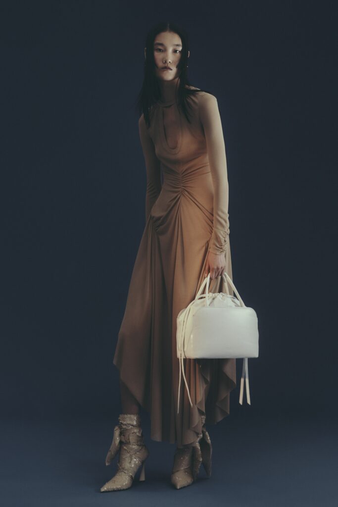 A fitted beige silk dress with a high neckline and draped detailing.