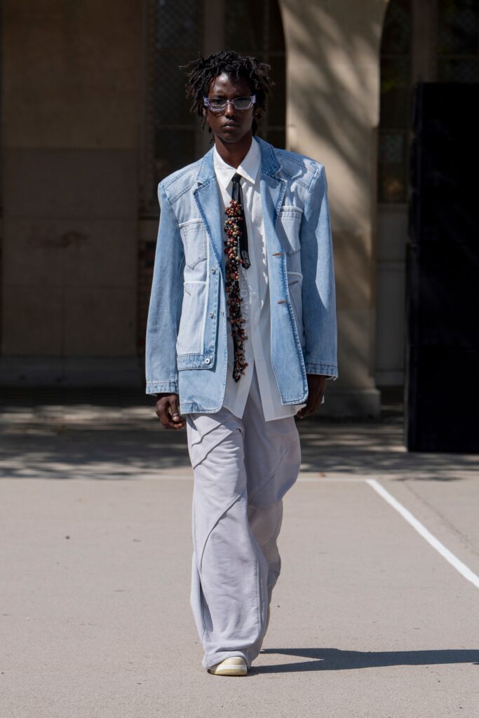 A relaxed blue denim jacket paired with collared shirt and straight-leg gray pants.
