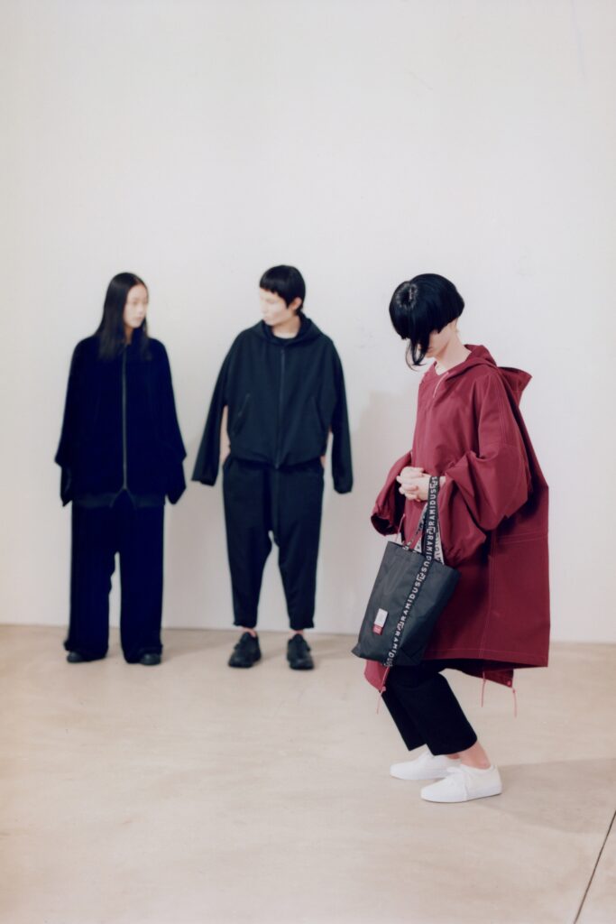 A relaxed burgundy cotton coat with a hood and asymmetric design details.