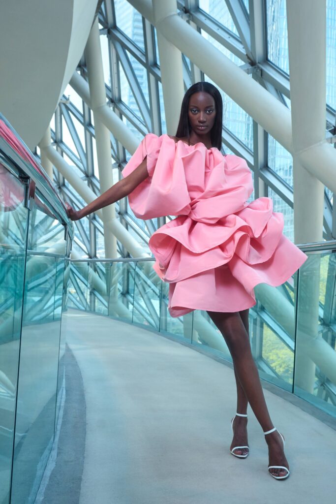 A fitted pink silk dress with a sleeveless high-neck design and ruffled details.