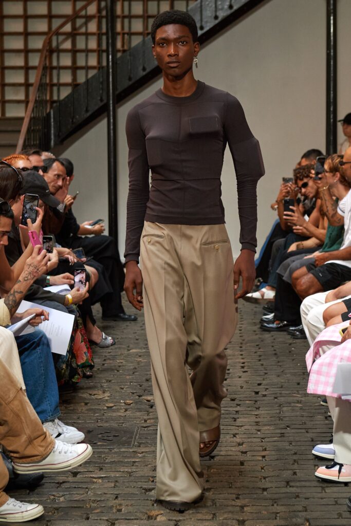 A fitted black long-sleeve top paired with straight-leg beige pants.