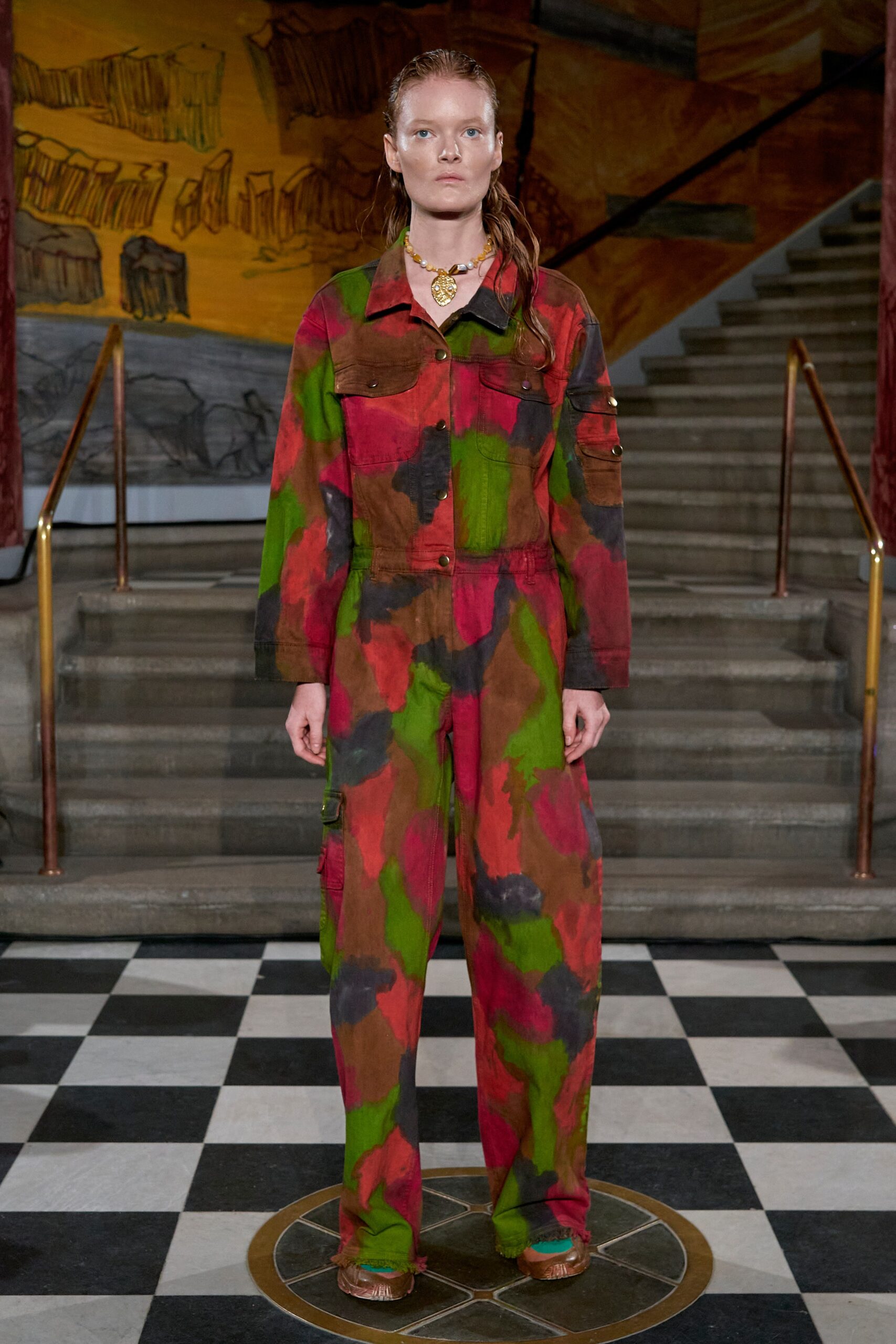 A relaxed jumpsuit featuring a vibrant print in red, green, and brown with long sleeves and a collared design.