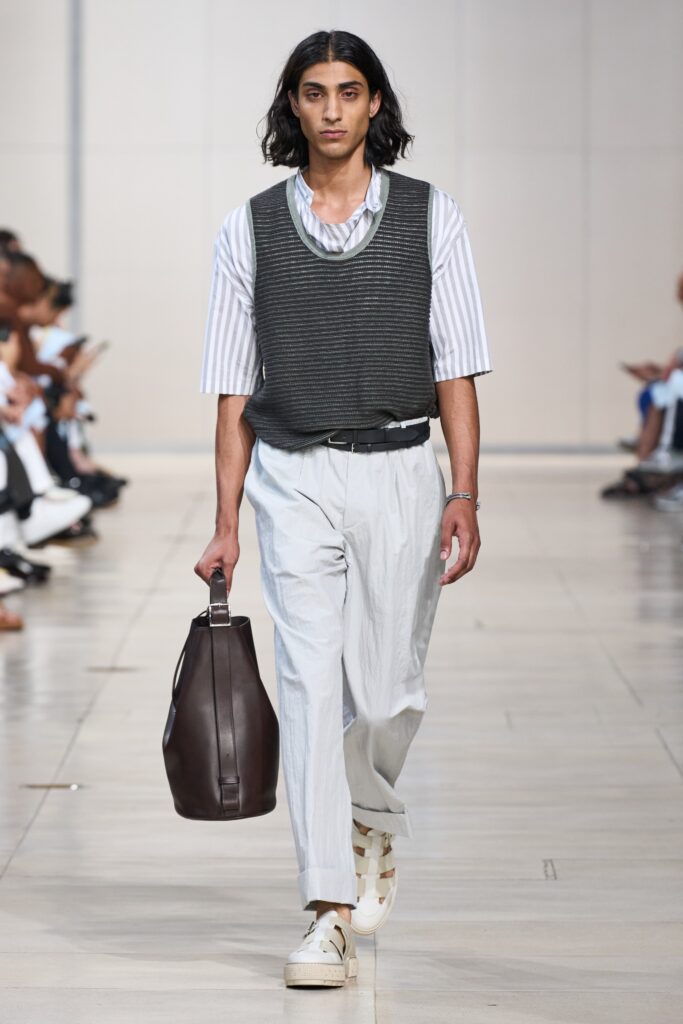 A relaxed white striped shirt layered with a gray vest, featuring pleated trousers.