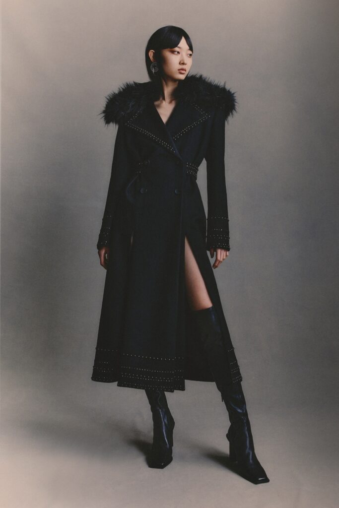 A fitted black leather coat with long sleeves, a collared neckline, and an asymmetric slit detail.