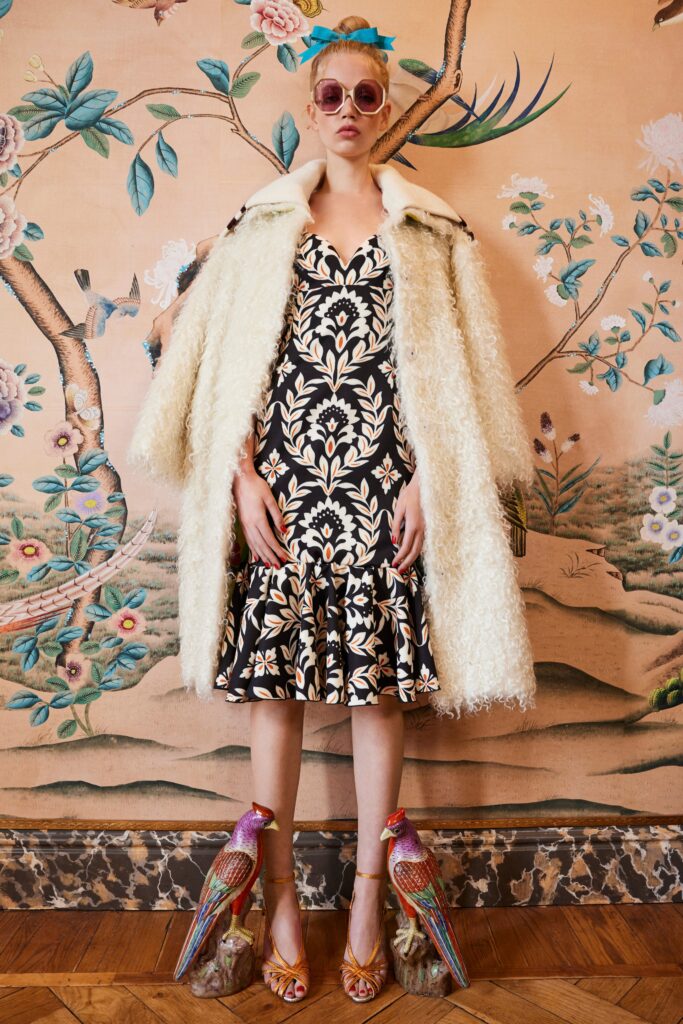 A fitted black dress with a flared silhouette, paired with a cream fur coat.