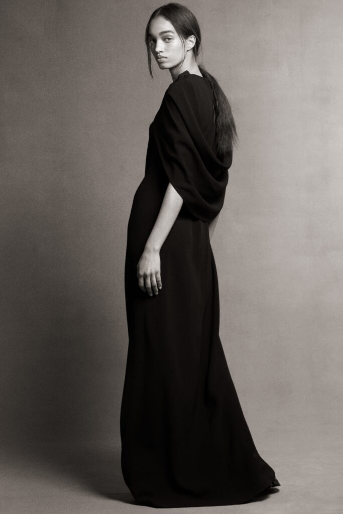 A relaxed black silk dress with long sleeves and a high neckline featuring a draped design.