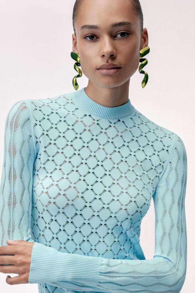 A fitted blue knit top with long sleeves and a high neckline featuring a sheer design.