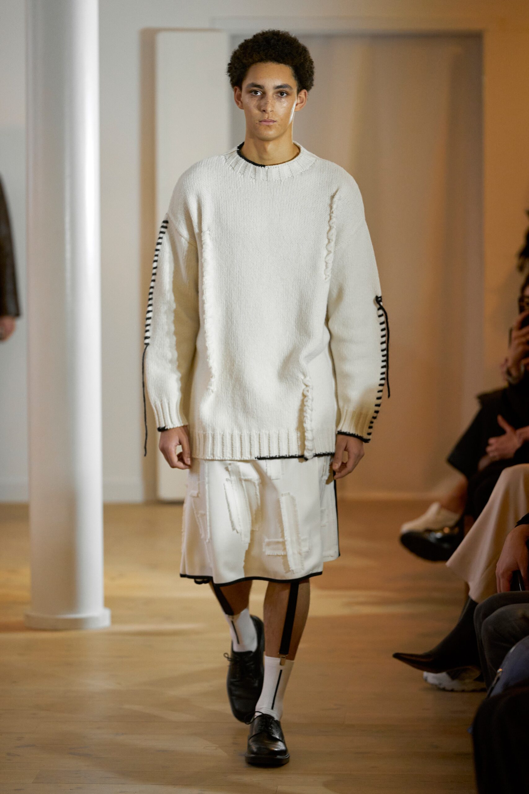 An oversized white cotton sweater with long sleeves paired with an asymmetric skirt.