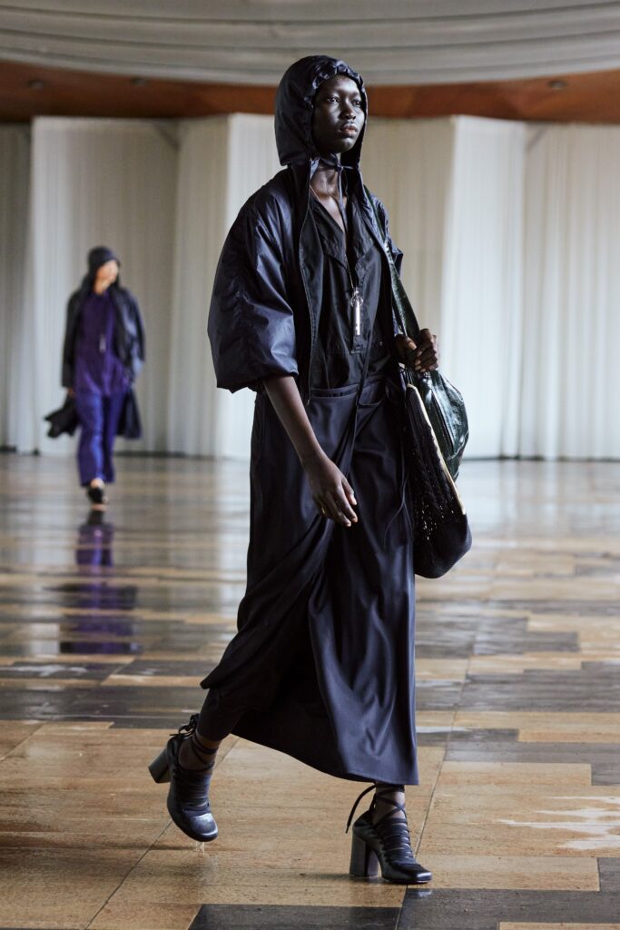A relaxed black dress with long sleeves and a hood, featuring a layered design.
