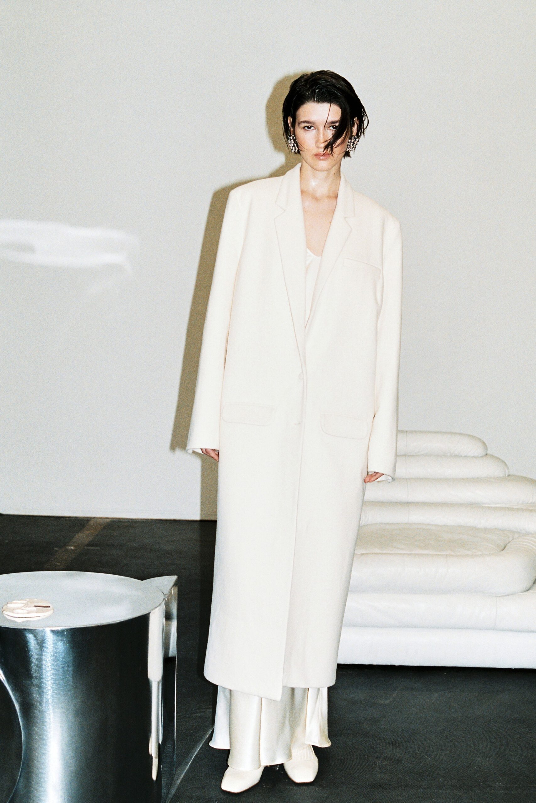 A relaxed white coat layered over a silk dress with a collared neckline.