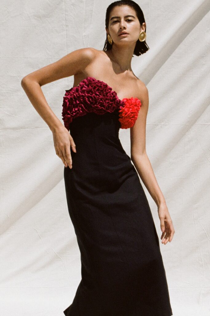A fitted black sleeveless dress featuring vibrant floral embellishments and a flared silhouette.