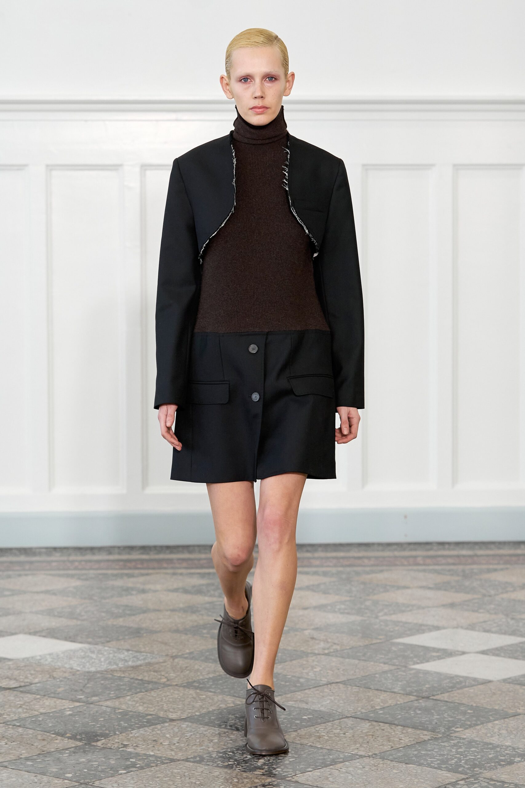 A fitted black dress paired with a black jacket featuring an asymmetric design and button details.