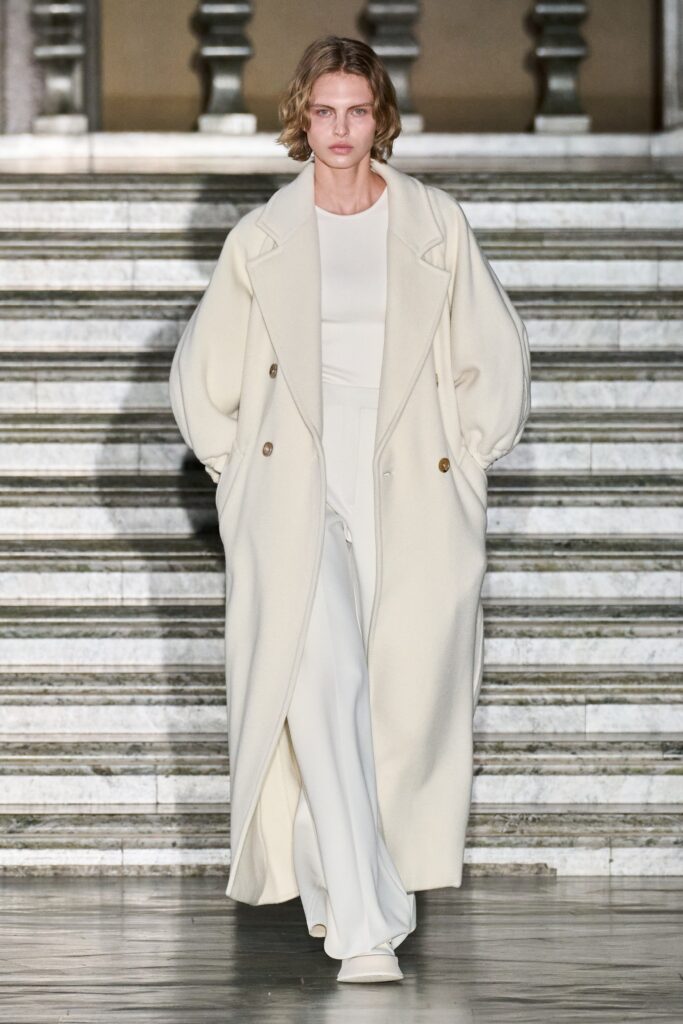 A relaxed white wool coat with long sleeves and a collared design, featuring button details.