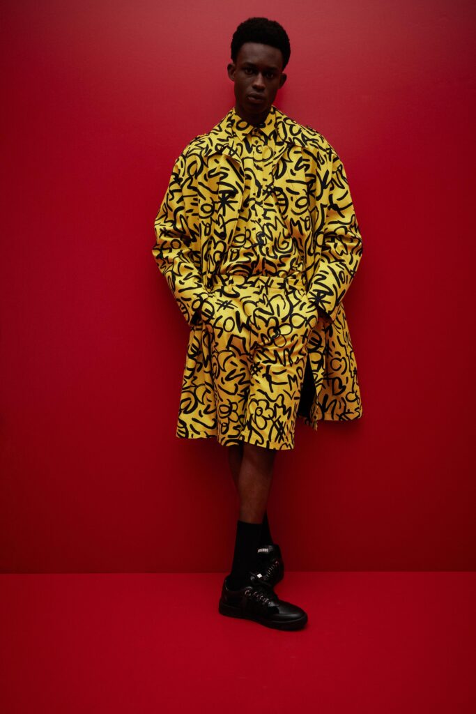 This relaxed ensemble features a striking yellow coat adorned with bold black prints, complemented by matching shorts. The long sleeves and collared design create a cohesive look that plays with proportions and visual impact.