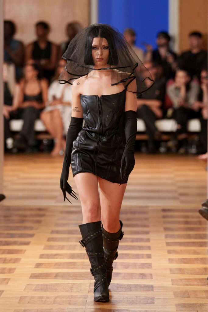 A fitted black leather sleeveless dress with a unique design and striking accessories.
